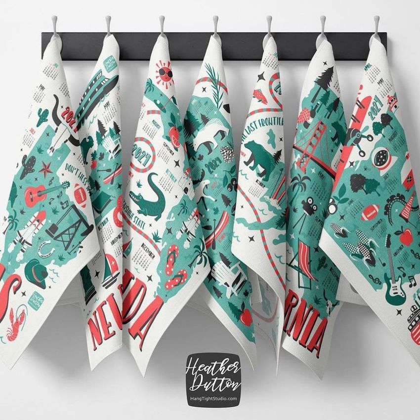 Hanging tea towels mockup showing seven towels with colorful state-themed graphics in teal and red on a black rod against a white wall.