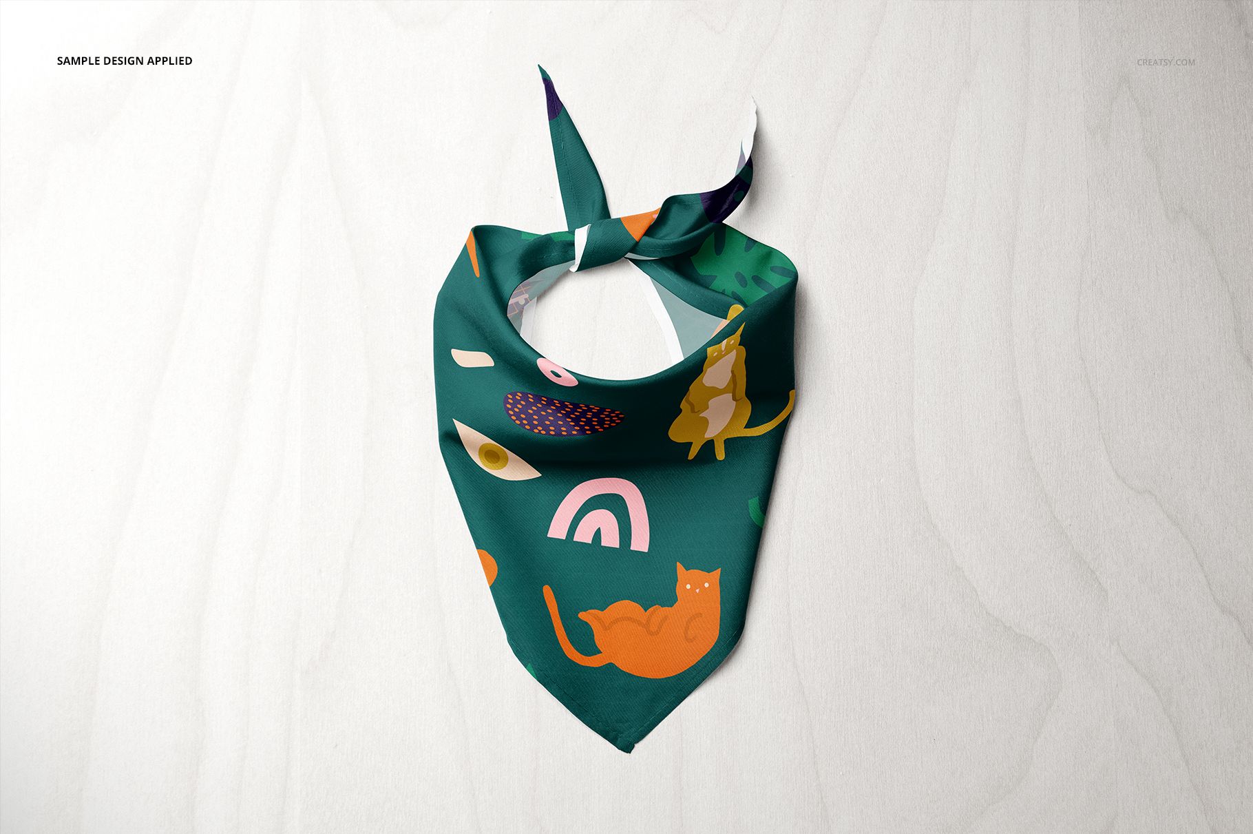 Pet bandana mockup featuring a green fabric with playful cat and rainbow patterns, shown from above on a pale background.