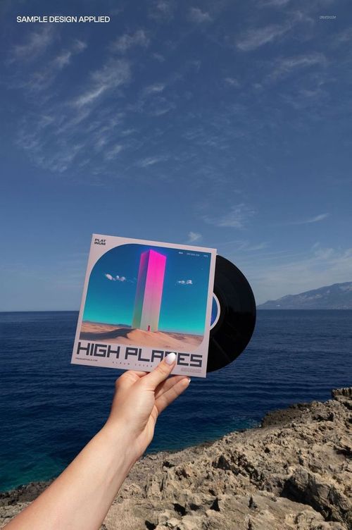 Black vinyl record mockup held up outdoors, with cover artwork and scenic sky and water visible behind.