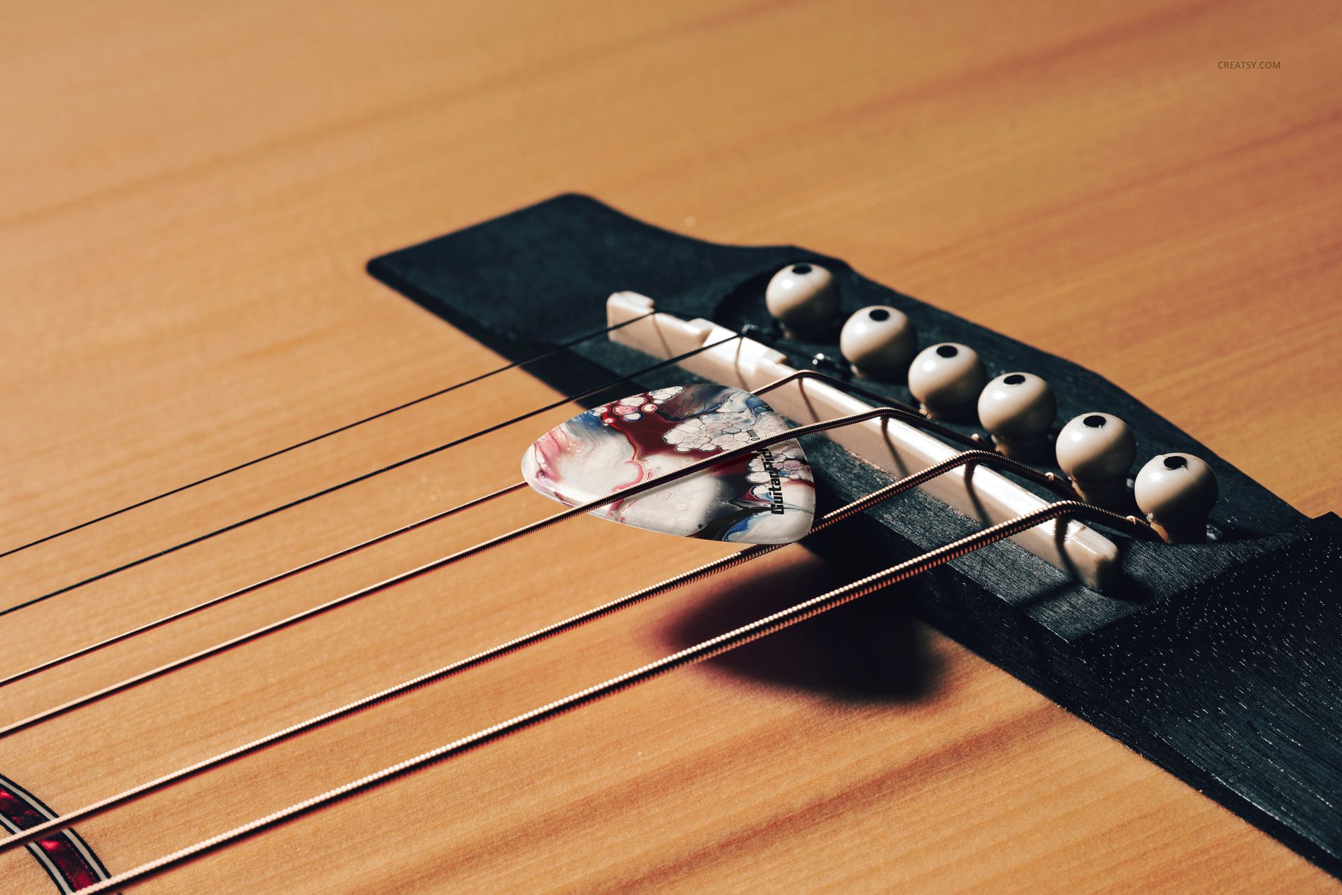 Detailed PSD mockup featuring a guitar pick positioned under the strings near the bridge of a natural wood acoustic guitar.