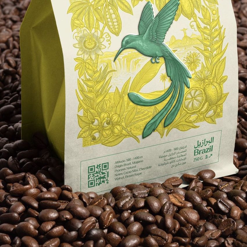 Coffee bag mockup featuring a green and yellow illustrated bird and botanical design, surrounded by roasted coffee beans.