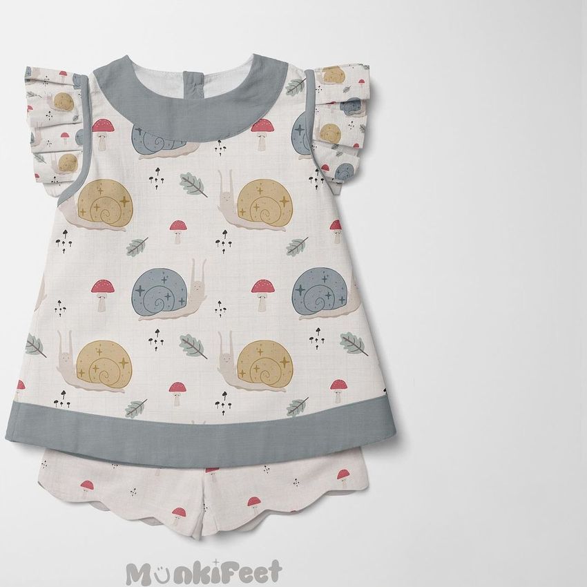 Kids blouse and shorts mockup featuring a snail and mushroom pattern in muted colors on a light background, shown flat on white.