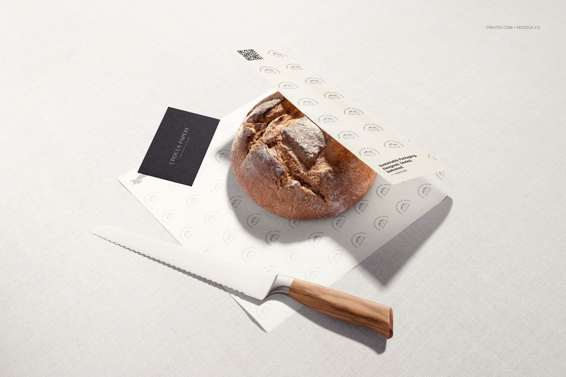 Mockup scene featuring a rustic bread loaf on branded food paper, knife with wooden handle, and minimalist background.