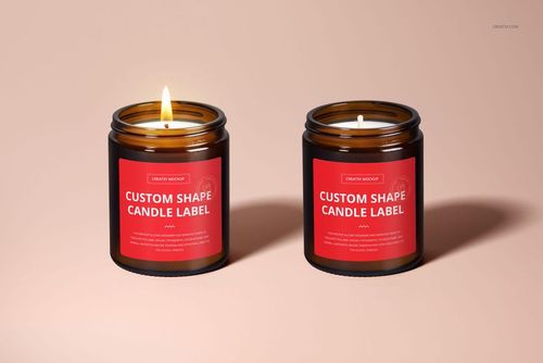 Two amber glass candles with cotton wicks and red labels, shown side by side on a beige surface in a PSD mockup.