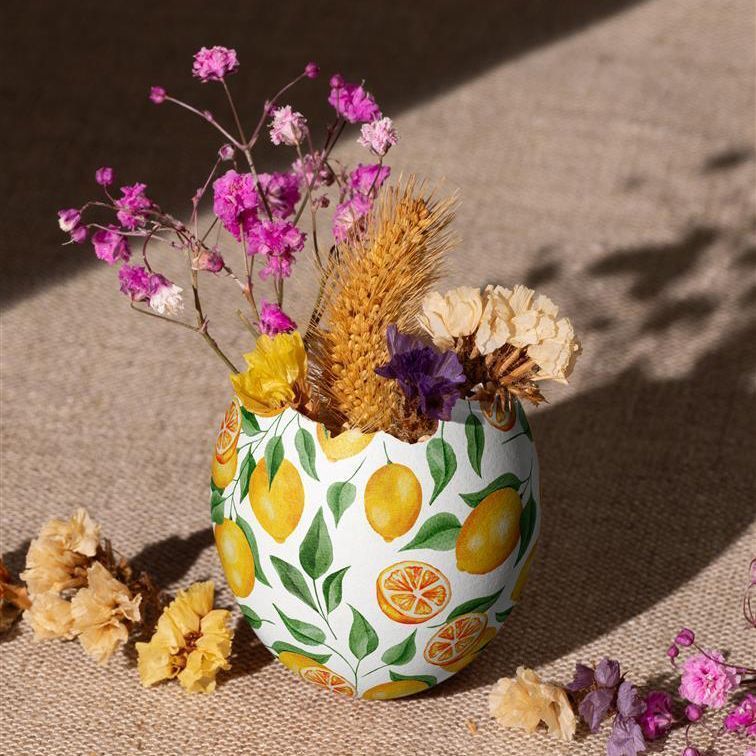 Painted Easter egg shell mockup featuring a lemon and leaf pattern, used as a vase for dried flowers on a fabric surface.
