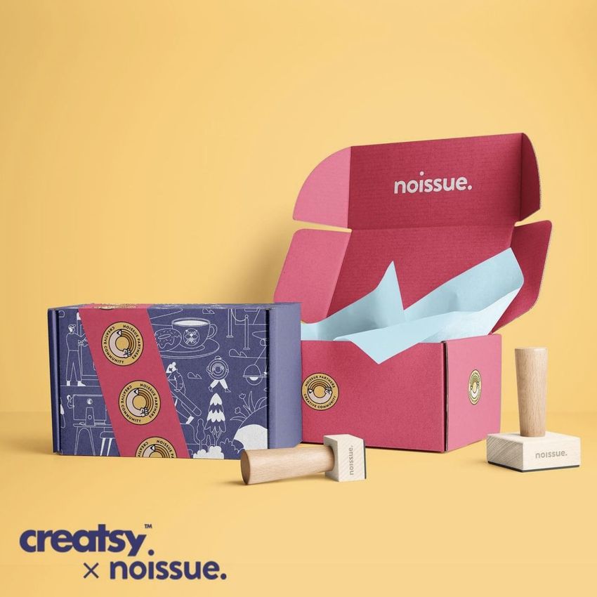 Mailing box mockup with two colorful boxes, one closed and one open with tissue paper inside, set on a yellow background with rubber stamps.