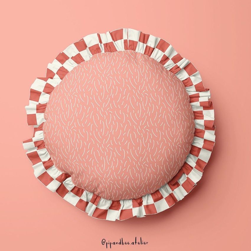 Round ruffled pillow mockup on a solid peach background, featuring a pink patterned surface and striped ruffle edge.