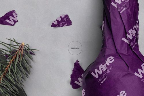 PSD mockup of a wine bottle wrapped in purple tissue paper with white print, top view with pine branch accent.