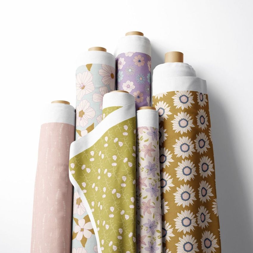 Fabric rolls mockup featuring six upright rolls with floral and botanical patterns in pastel pink, green, yellow, and purple tones.