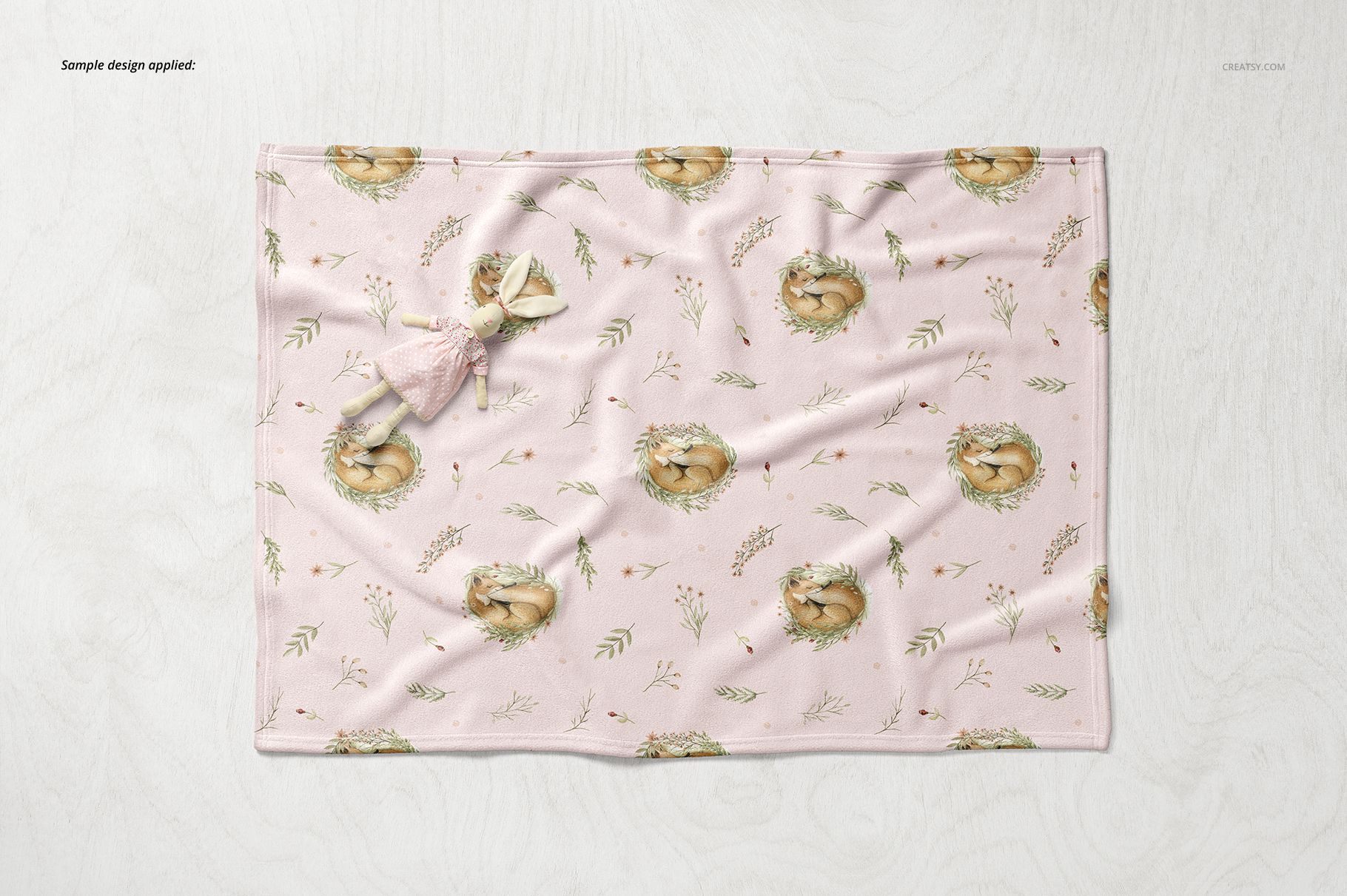 Baby blanket mockup featuring soft fleece material, pink color, and animal illustrations, displayed flat with a doll.