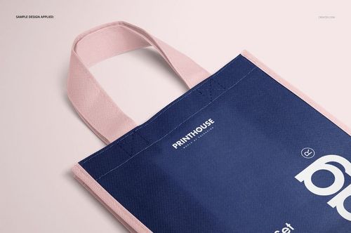 Close-up of a non-woven tote bag mockup with pastel pink handles and border, dark blue body, angled from above.