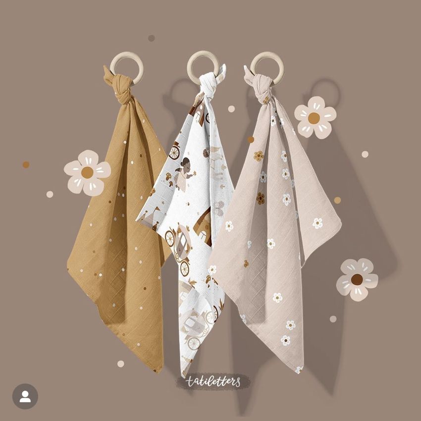Muslin cloth wooden teether mockup showing three cloths in earthy tones and patterns, hanging on wooden rings against a brown background.