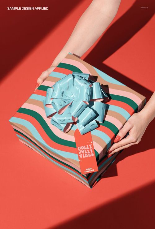 Square magnetic box mockup featuring bold striped design, shiny blue bow, and red label, held by hands over a red backdrop.