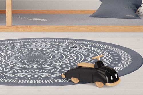 Round rug with geometric white pattern, black wooden toy car, and lower half of a kids bunk bed in a bedroom mockup.