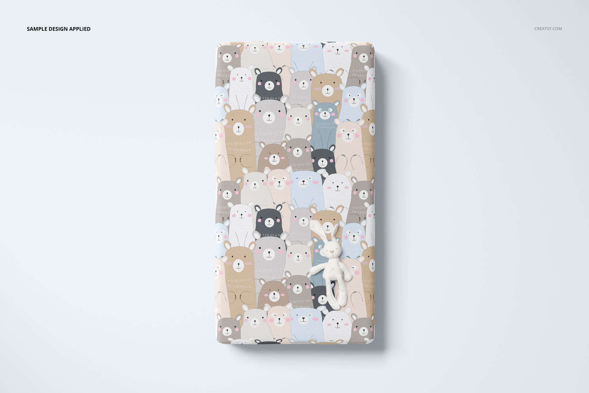 Crib sheet mockup with a cute multicolored bear design, shown from above with a plush toy on a white background.