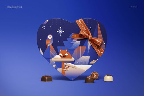 Front view of heart-shaped chocolate box mockup featuring a fox and owl design, orange ribbon, blue backdrop, chocolates in front.
