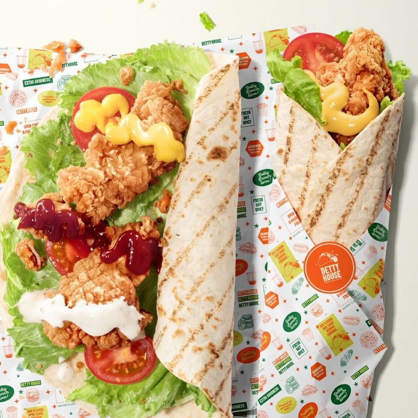 Food safe paper mockup showing a grilled tortilla wrap with fried chicken, lettuce, tomato, and sauces on colorful printed packaging.