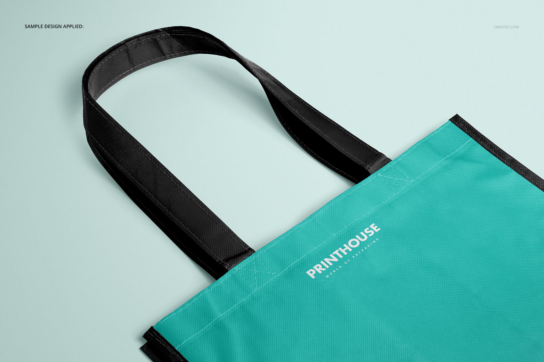 Front angled view of a laminated non-woven tote bag mockup with black handles and a turquoise body on a light surface.