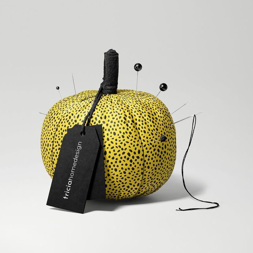 Fabric pumpkin mockup with a yellow and black spotted pattern, black stem, and sewing pins, set on a light gray background.