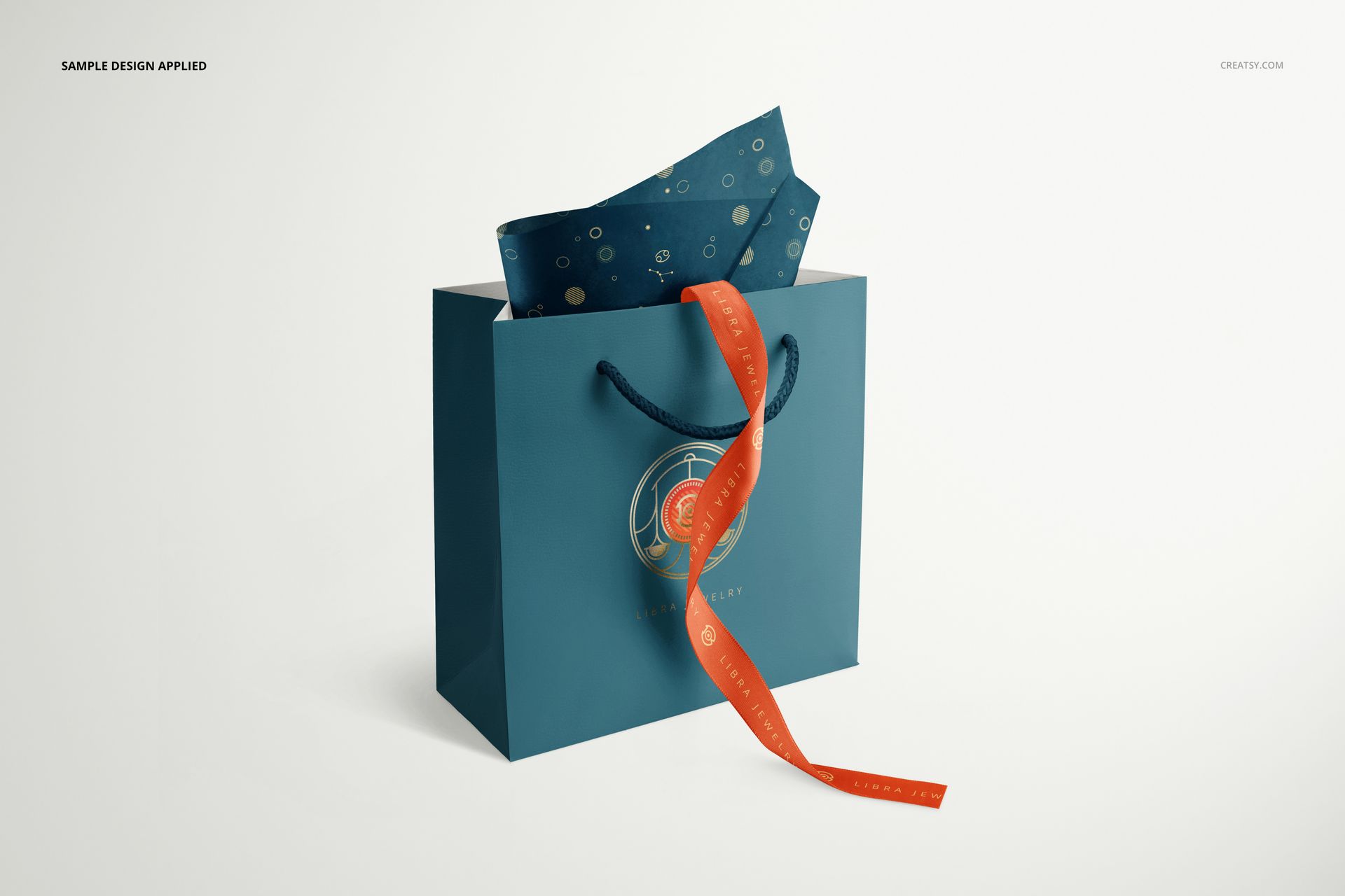 Front view of a blue jewelry box bag with circular logo, orange ribbon, and dark blue tissue paper mockup.