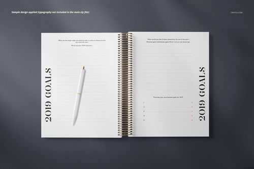 PSD mockup of an open coil bound planner featuring lined pages, black typography, and a white pen on a gray background.