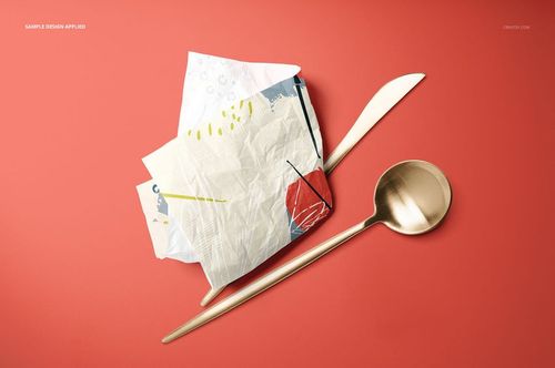 PSD mockup of folded and crumpled napkins with modern prints, arranged with a spoon and knife on a vibrant red tabletop.