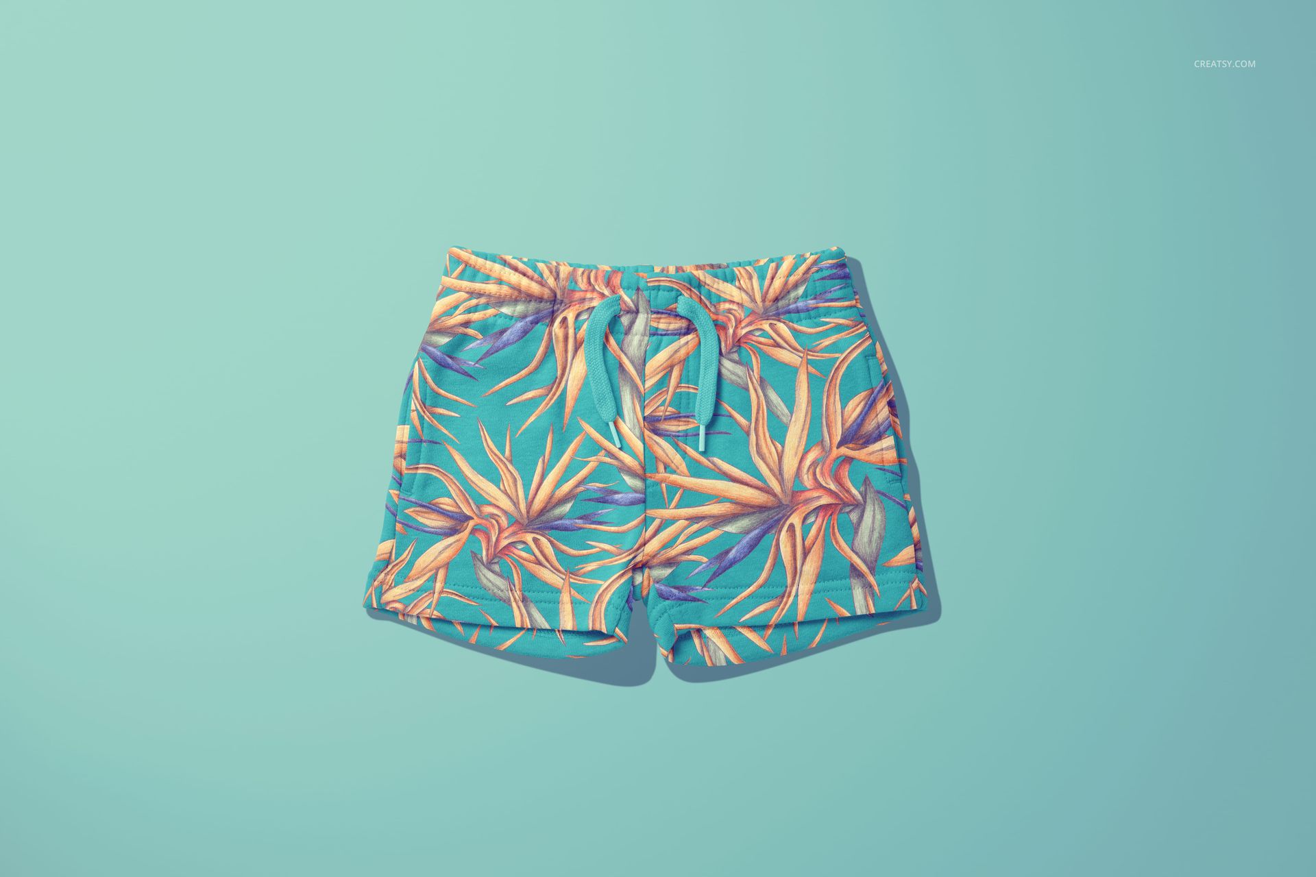 PSD mockup of children's shorts with colorful botanical design, laid flat against a light blue background.