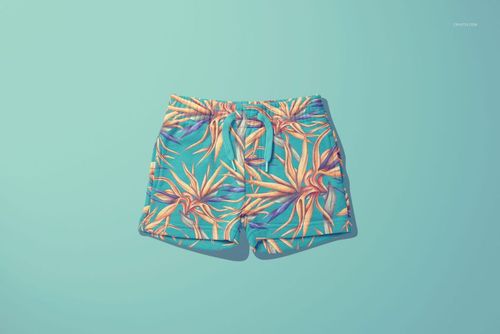 PSD mockup of children's shorts with colorful botanical design, laid flat against a light blue background.