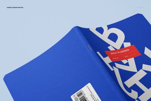 Opened notebook mockup showing a blue cover with large white text and a red label, viewed from an angled perspective.