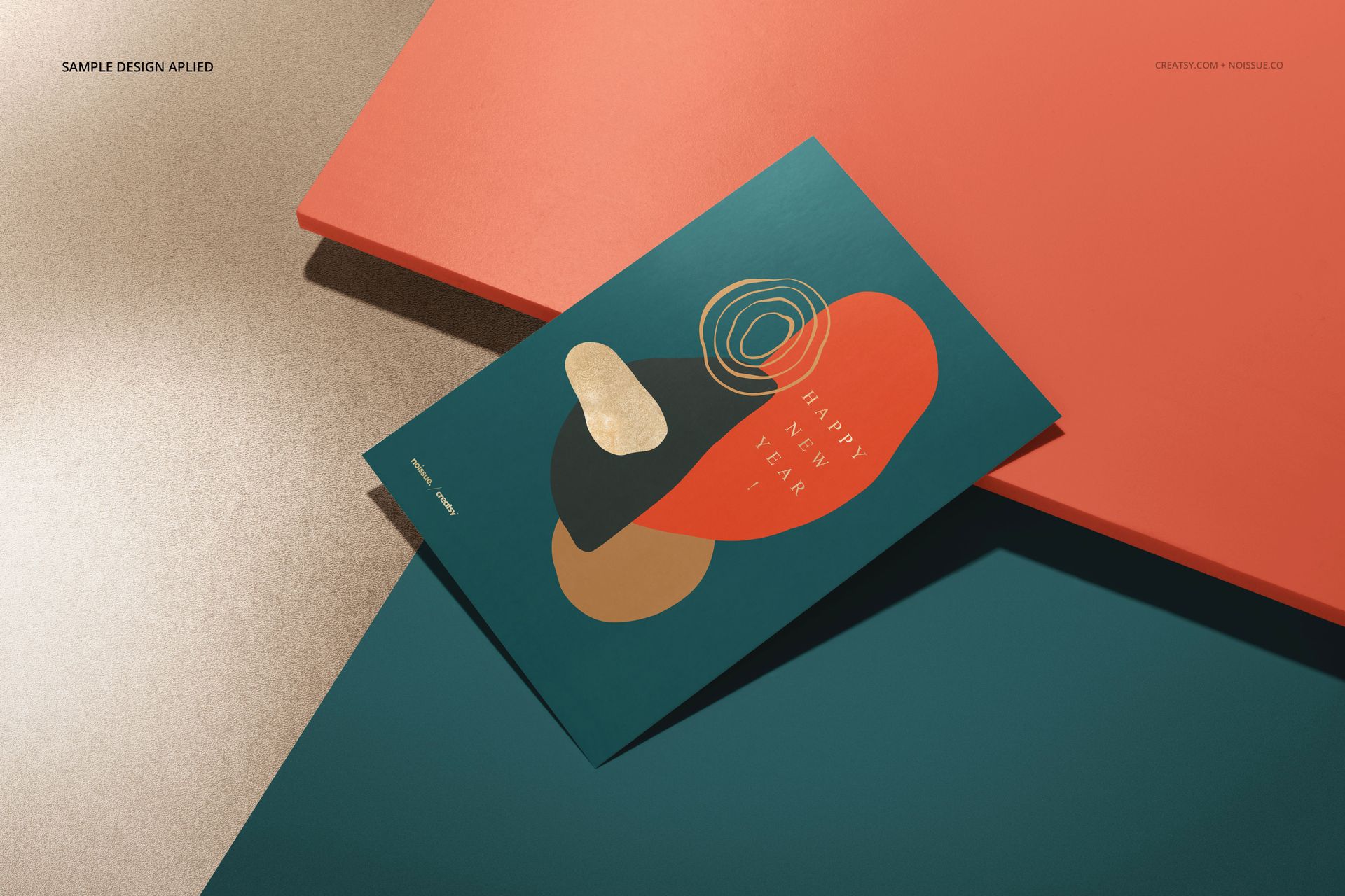 Stationery card mockup with abstract geometric design in gold, coral, and teal, shown on colored surfaces.