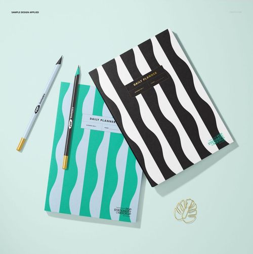 Stationery mockup showing two planners with bold wavy designs, teal and black covers, pencils, and a gold paperclip.