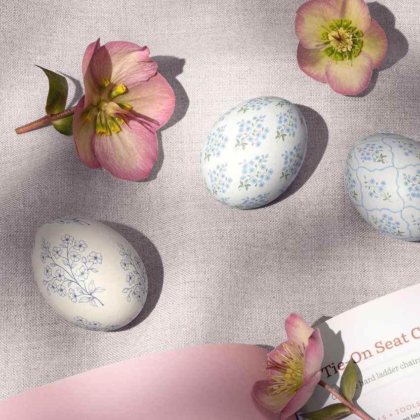 Book and Easter eggs mockup featuring three decorated eggs with blue floral patterns, pink flowers, and an open book on a light fabric background.