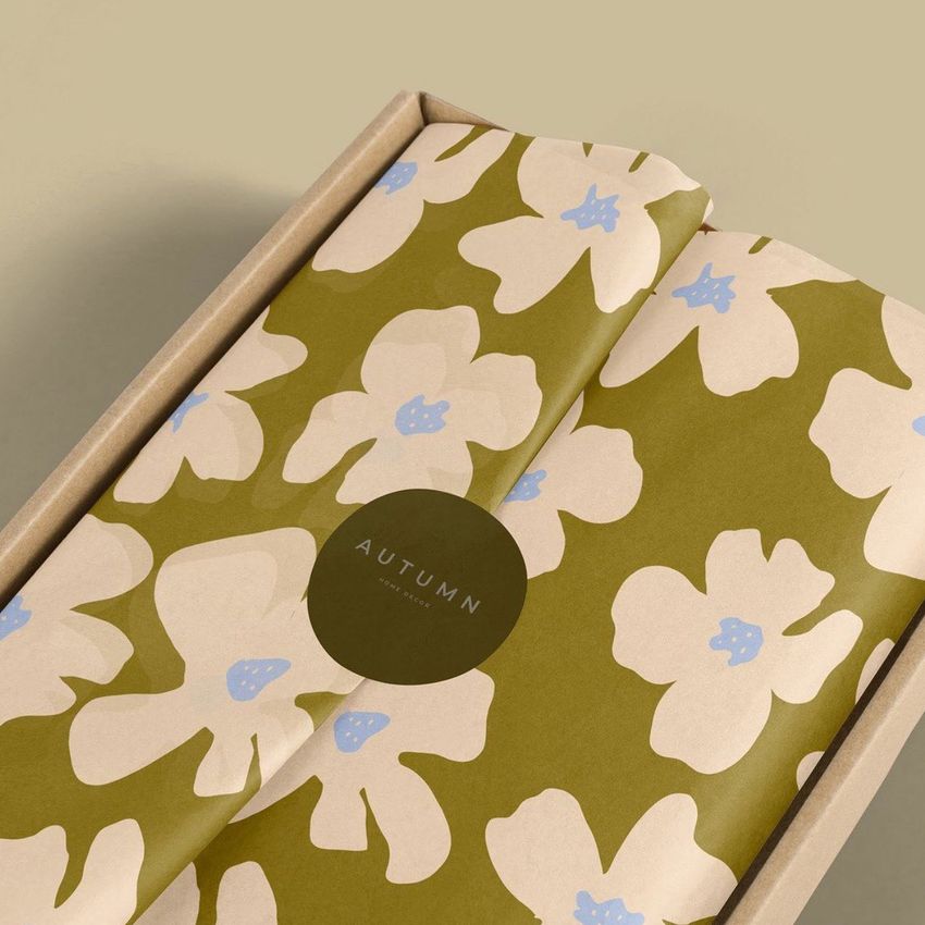 Mailer box mockup with olive green tissue paper featuring large cream and blue floral patterns, viewed from above on a beige background.