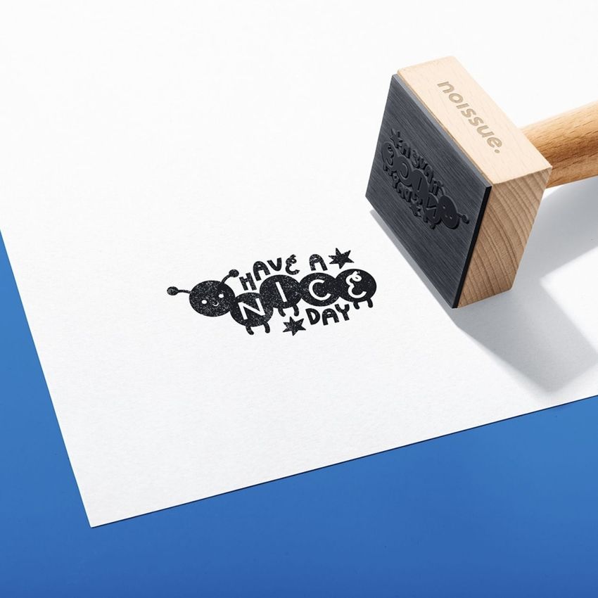 Wooden stamp mockup set on white paper with a playful black ink design and bold text, placed on a blue surface.