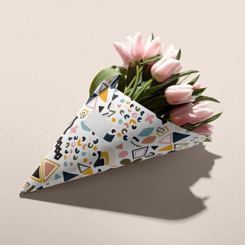 Flowers packaging cone mockup featuring pink tulips wrapped in a cone with colorful geometric patterns on a beige surface.