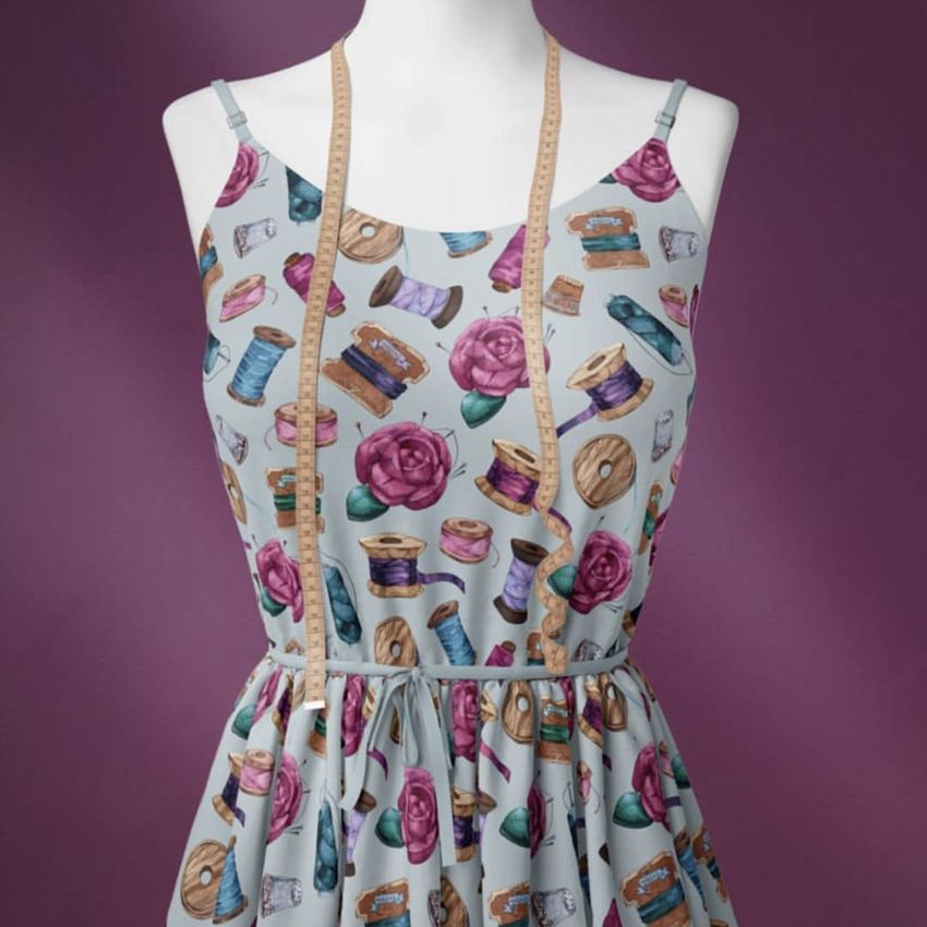 Fabric dress mockup featuring a sleeveless dress with a sewing-themed pattern, displayed on a mannequin against a purple background.