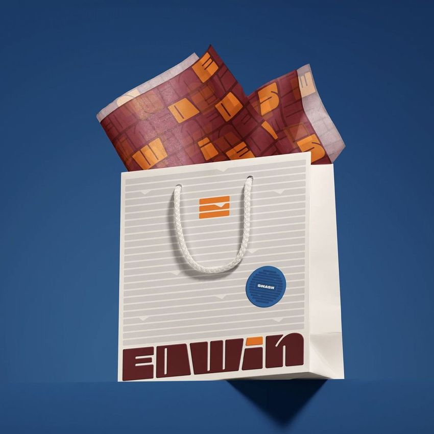 Shopping bag mockup with white rope handles, geometric text design, and patterned tissue paper on a blue background.