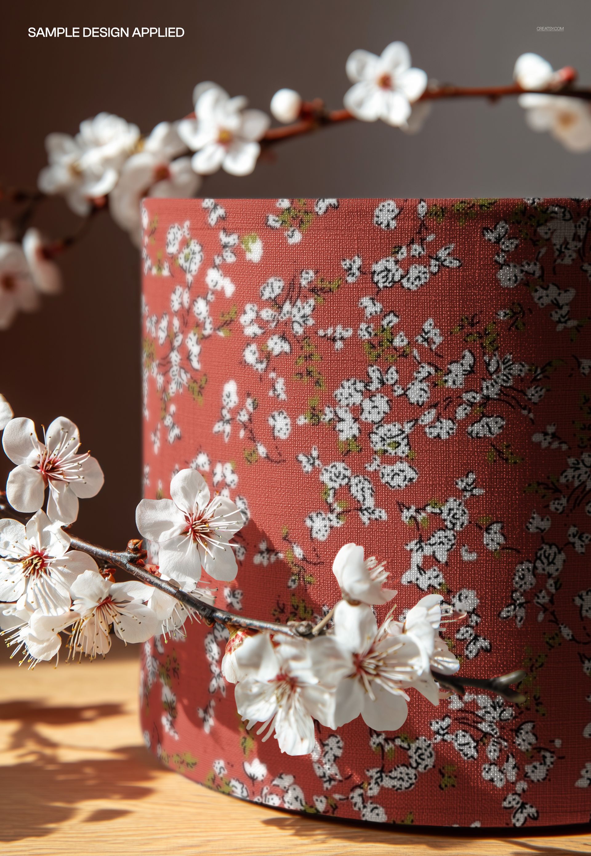 PSD mockup of a cylindrical lampshade featuring a red background with white blossom branches, photographed close-up.