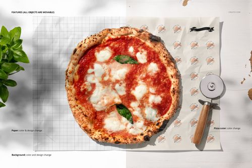 Pizza on branded food safe paper mockup, viewed from above, with a pizza cutter and green leaves on a white table.