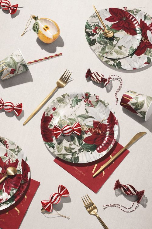 Disposable Christmas tableware mockup featuring plates, cups, and cutlery with red and green festive floral patterns.