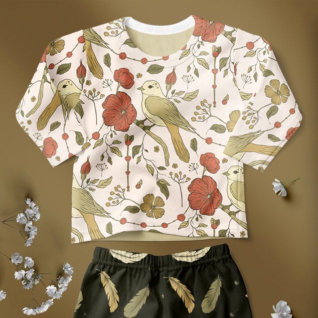 Baby long sleeve pyjama mockup featuring a cream top with a bird and flower pattern and dark pants with feather prints, displayed on a brown background.