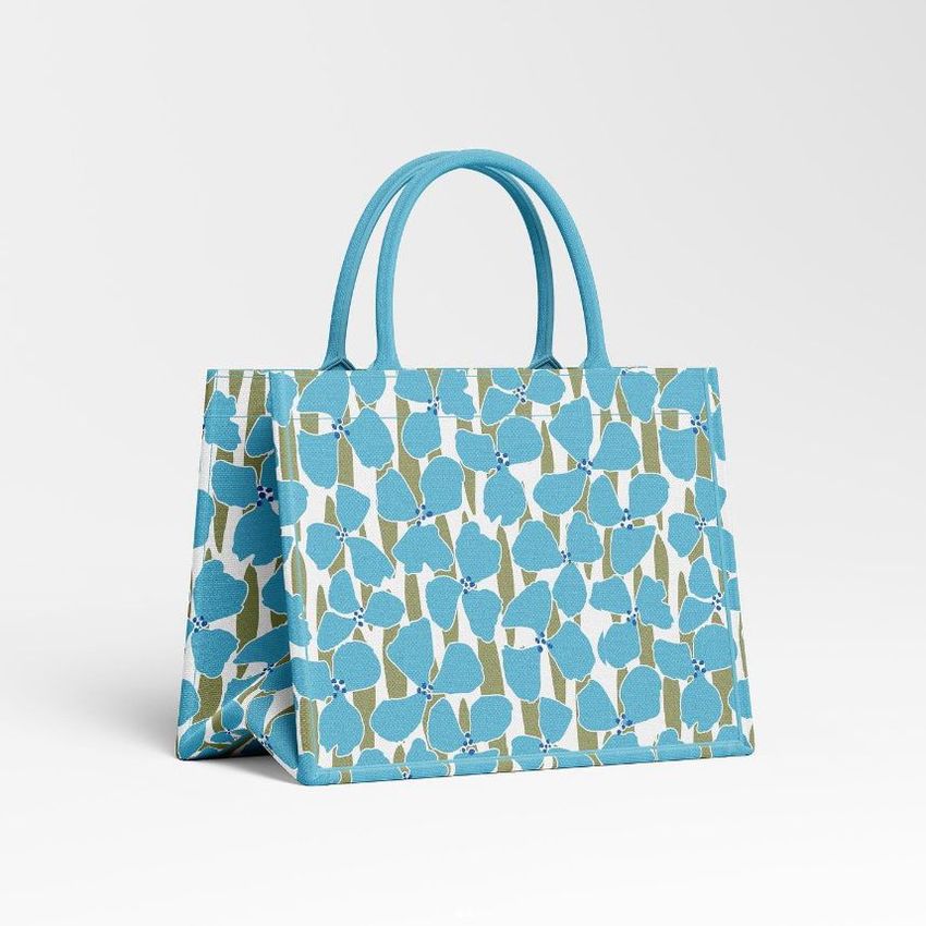 Canvas tote bag mockup featuring a blue and green floral pattern, standing upright on a light gray background.
