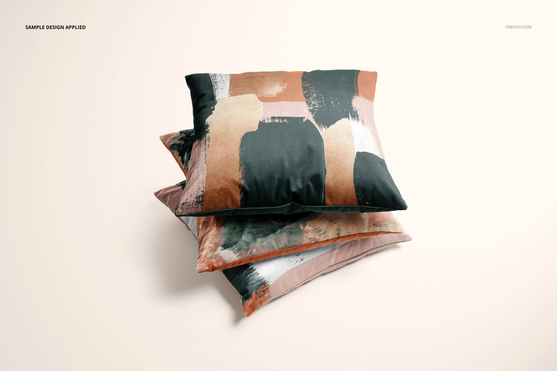 Velvet pillow mockup set showing three cushions with bold, painted designs in earthy colors arranged on a light surface.