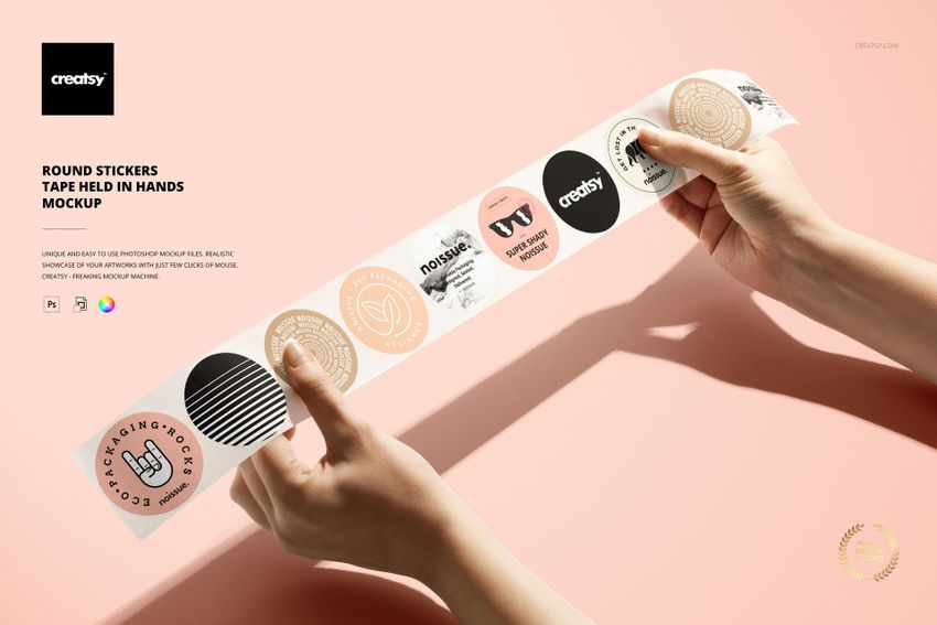 PSD mockup showing hands holding a tape of round stickers with assorted designs and pastel tones on a neutral surface.