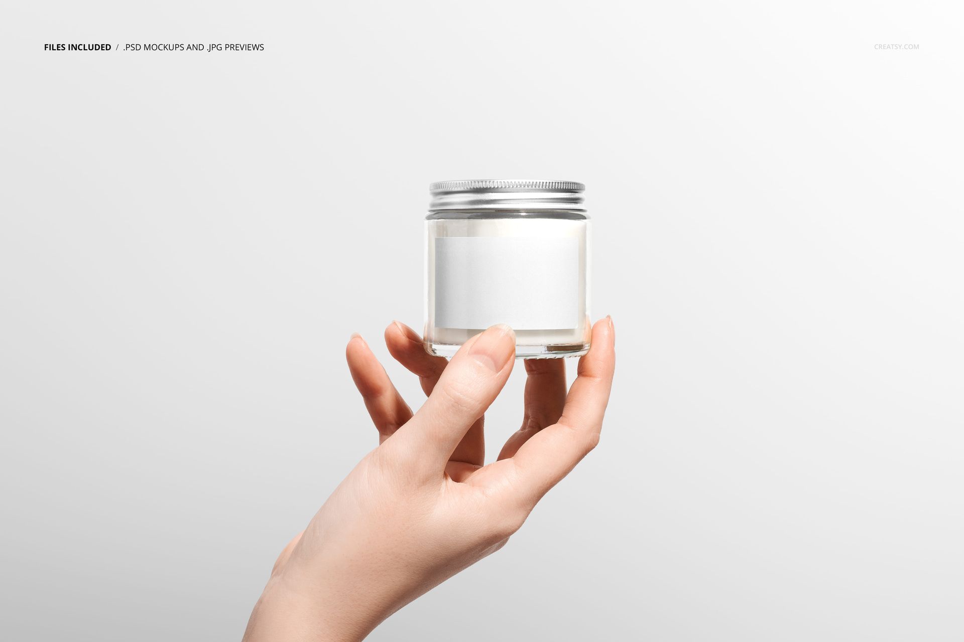 Minimalist scene featuring a hand grasping a transparent candle jar, silver screw top, and blank label, PSD mockup style.
