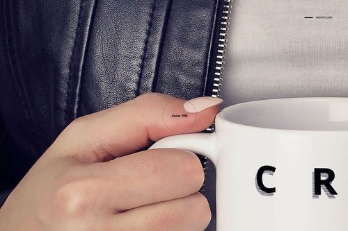 Close-up front view of a hand holding a plain white ceramic mug, with part of a black leather jacket and zipper visible.