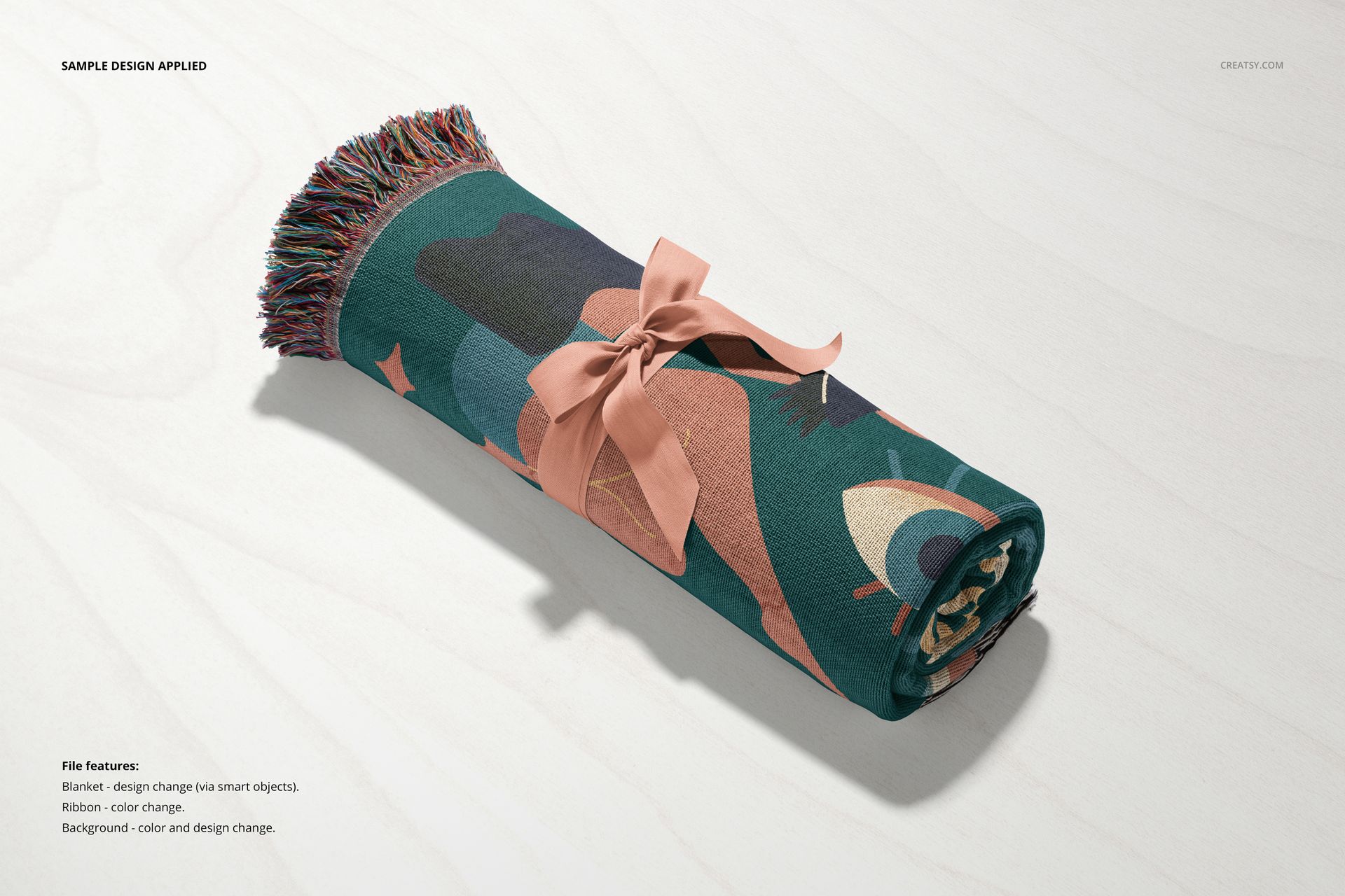 Jacquard fringed throw blanket mockup rolled up, featuring a bold abstract pattern and pink ribbon on a light surface.