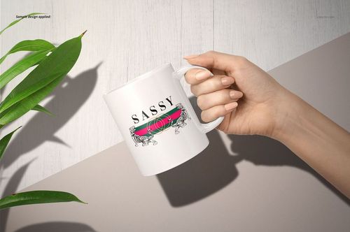 Hand holding a white 11oz mug with a decorative text design, viewed from the side on a light background.