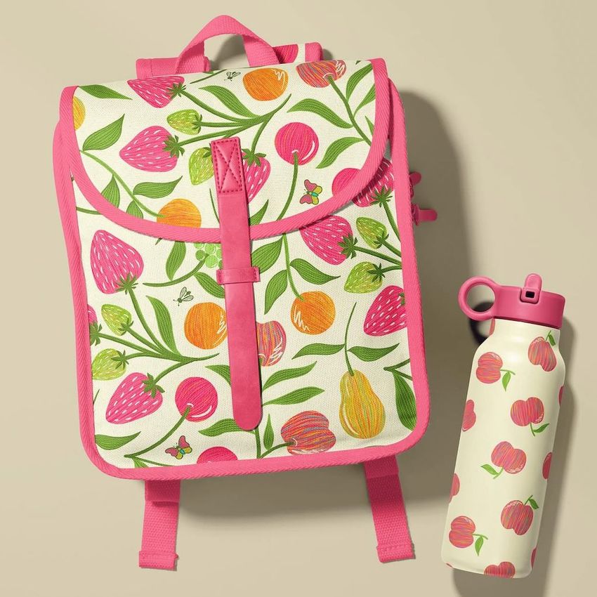 Kids backpack mockup with bright pink straps and a playful fruit pattern, shown next to a matching water bottle on a beige surface.
