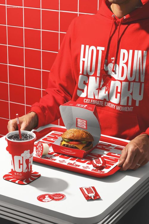 Person in a red hoodie sits at a burger bar table with a tray holding a burger, drink, fries, and packaging mockup.